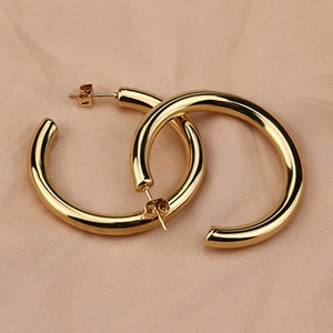 Close-up of golden geometric hollow hoop earrings with high-polish mirror finish and ear studs