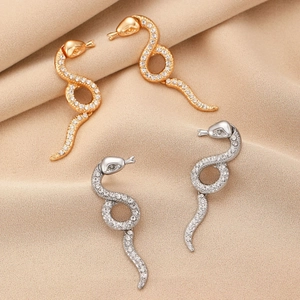 Elegant gold and silver snake earrings with white zircons on beige pleated silk backdrop