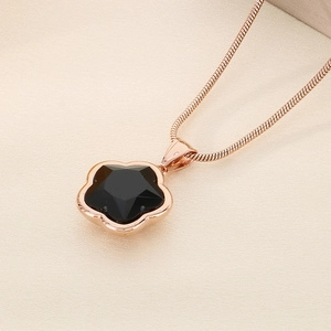 Macro shot of rose gold snake chain necklace with black five-petal flower clover pendant