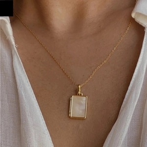 Close-up of a gold rectangular locket necklace with white shell inlay on a female model