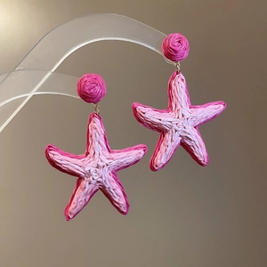 Close-up of pink starfish drop earrings with gradient woven texture on a clear display