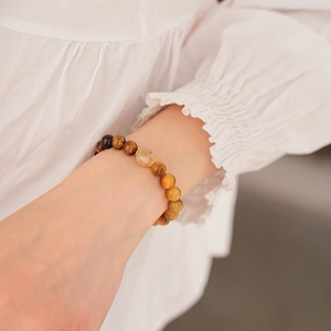 Detail of beaded tiger eye bracelet with gold accents on woman's wrist with ruffles