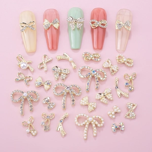 Golden alloy bowknot nail art set with rhinestones and pearls on pink background