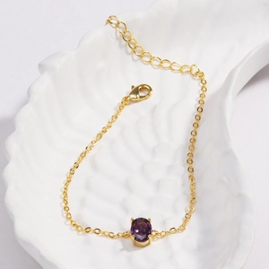 Close-up of gold-plated bracelet with purple oval zircon stone on a white shell tray