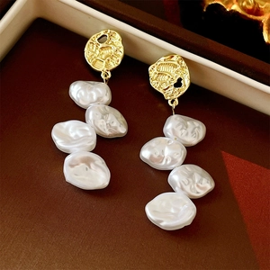 Detailed close-up of long baroque pearl earrings with textured gold metal accents