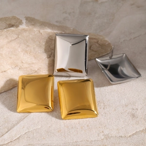 Detailed view of polished gold and silver rectangular stud earrings on stone background