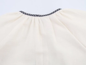 Close-up of cream shirt neckline with decorative black and white wavy embroidered edges