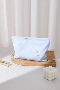Détail d'une trousse de maquillage à rayures bleues avec broderie nœud et étiquette H&R BAG