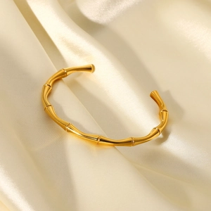Détail d'un bracelet ouvert doré à texture bambou sur fond de soie champagne
