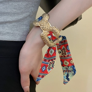 Detail of gold snake-textured open cuff bracelet with red printed silk scarf wrap
