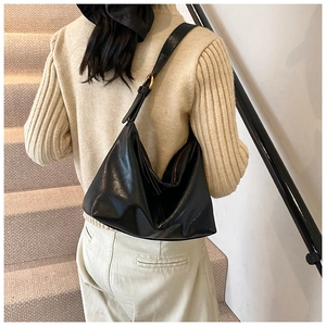 Close-up of black glossy hobo bag with golden adjustable buckle on leather strap