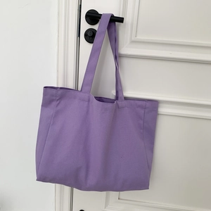 Detail view of a large purple canvas tote bag hanging on a door with wide shoulder straps