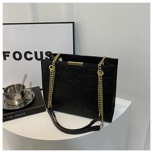 Detail of black quilted tote bag with hexagonal pattern and gold chain strap