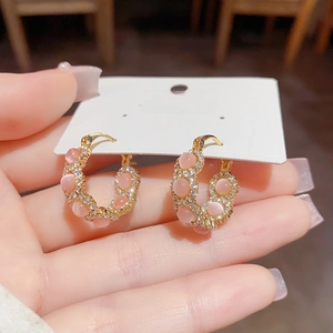 Detail of gold hoop earrings with pink cat eye stones and sparkling white zircons