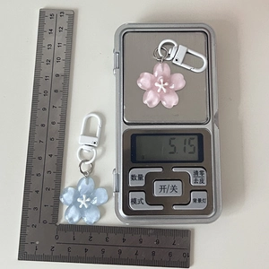 Detail showing pink and blue cherry blossom keychains on scale weighing 5.15g