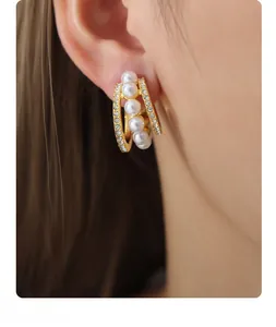 Détail de boucles d'oreilles en titane doré en C avec perles blanches et micro-cristaux