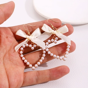Détail de boucles d'oreilles cœur avec nœuds en ruban beige et perles blanches dorées