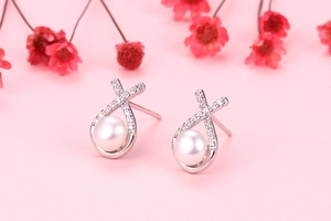 Macro view of S925 silver pearl stud earrings with zircon-set crisscross metal design