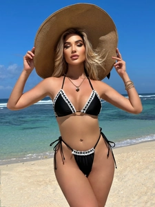 Sexy black bikini set with white lace trim shown on a tropical beach setting