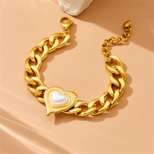 Golden Cuban link bracelet with pearl heart pendant on a beige stone background