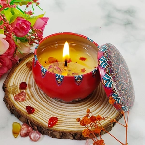 Scented candle in red mandala tin with dried petals and flame on wooden base