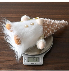 Detail view of a plush Christmas gnome on a scale showing its 121g lightweight design