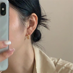 Close-up of a minimalist gold twisted hoop earring worn on an ear for size reference