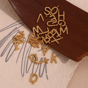 Detail of 18K gold plated alphabet pendants with twisted rope texture on wood