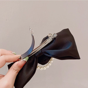 Close-up of black velvet bow hair clip with silver spring clasp and pearl tassel detail