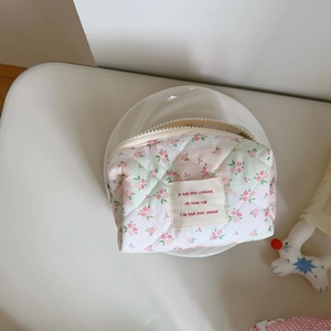 Close-up of pink floral quilted makeup bag with decorative fabric patch and white zipper