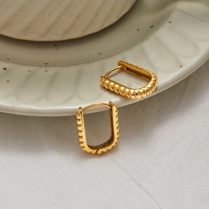 Textured gold U-shaped stainless steel earrings on a ceramic dish and linen cloth