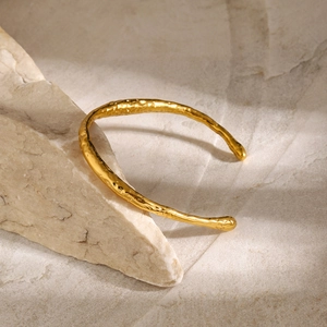 Detailansicht eines goldenen Edelstahl-Armreifs mit unregelmäßiger Hammerschlag-Textur auf Stein