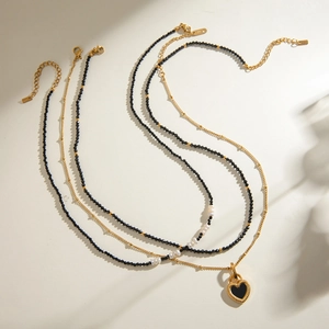 Layered gold chain necklace featuring black faceted beads and a black heart pendant