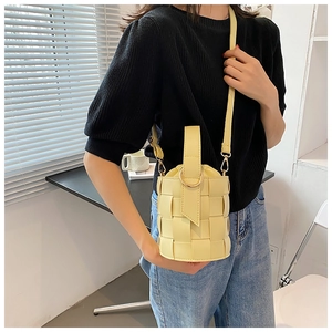 Detail view of woven light yellow bucket bag with gold hardware and a slim shoulder strap