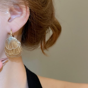 Close-up of golden layered leaf-shaped hoop earrings with hollow metal texture on model