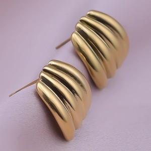 Macro view of textured golden shell-shaped earrings on light purple silk fabric
