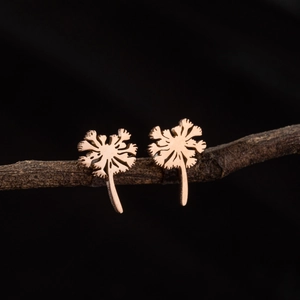 Rose gold dandelion earrings on a natural wood branch against a black background