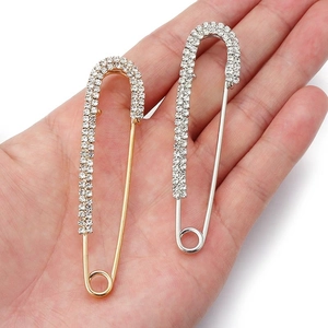 Detail view of crystal-encrusted gold and silver U-shaped safety pins held in hand