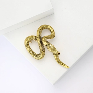 Golden python snake brooch with textured scales displayed on white geometric blocks