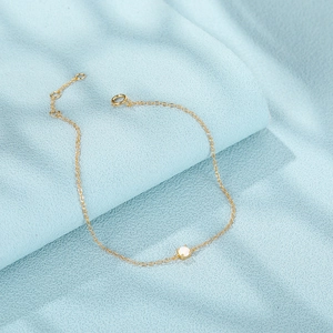 Detailansicht eines Goldketten-Armbands mit weißem quadratischem Stein auf blauem Stoff