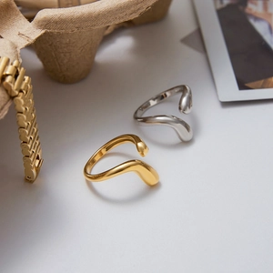 Close-up of polished gold and silver teardrop rings on a minimalist textured tray