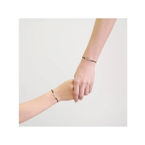 Gros plan de bracelets cordon noir réglables avec croix argentée portés par deux mains croisées