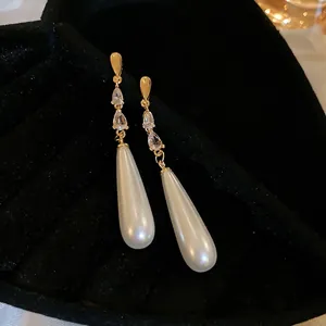 Élégantes boucles d'oreilles perles goutte dorées avec zircons sur fond velours noir
