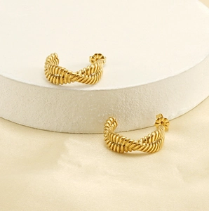 Close-up of twisted 18K gold plated C-shaped earrings on a neutral display stand
