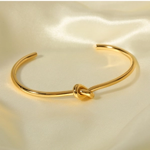 Dettaglio di un bracciale dorato con nodo su seta beige e illuminazione soffusa