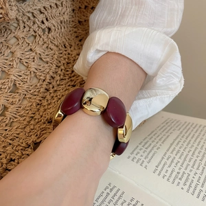 Close-up of chunky gold and burgundy acrylic pebble bracelet styled with a linen bag