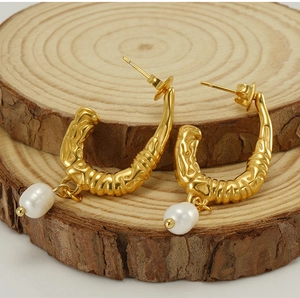 Vue détaillée des boucles d'oreilles dorées en U avec texture et perles blanches suspendues