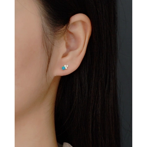 Close-up of a blue opal stud earring with gold finish on a model's ear with crystal accents