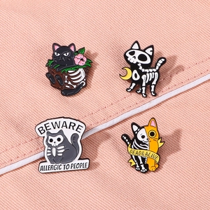 Set of four Halloween cat skull enamel pins on a pink textured fabric background