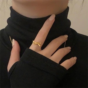 Detail of a gold bow ring in minimalist Korean style worn by a model on dark background